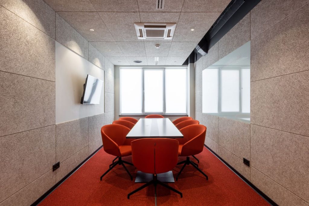 Orange chairs placed around white table in modern conference room with window and TV on wall in contemporary business center